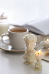 Beautiful David bust candles and cup of hot drink on  white table indoors, space for text