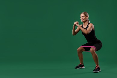 Photo of Smiling woman exercising with elastic resistance band on green background. Space for text