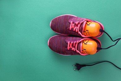 Pair of stylish sneakers with modern electric shoe dryer on green background, top view. Space for text