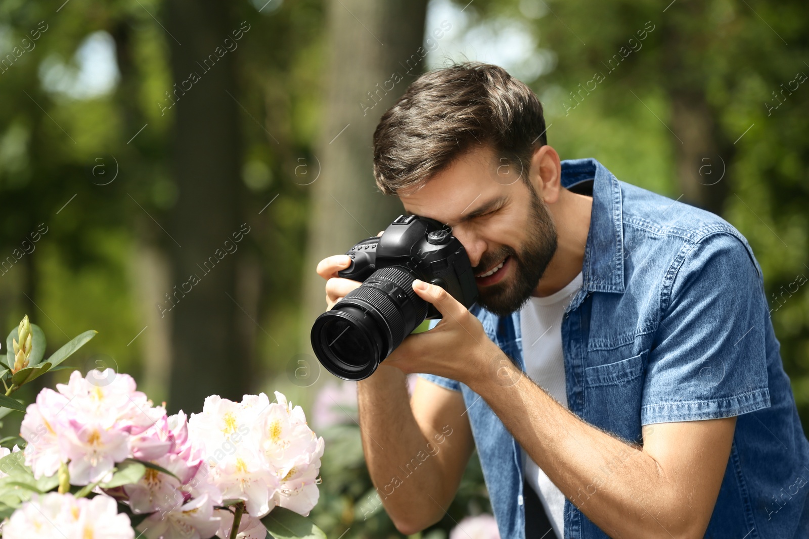 Photo of Photographer taking photo of blossoming bush with professional camera in park