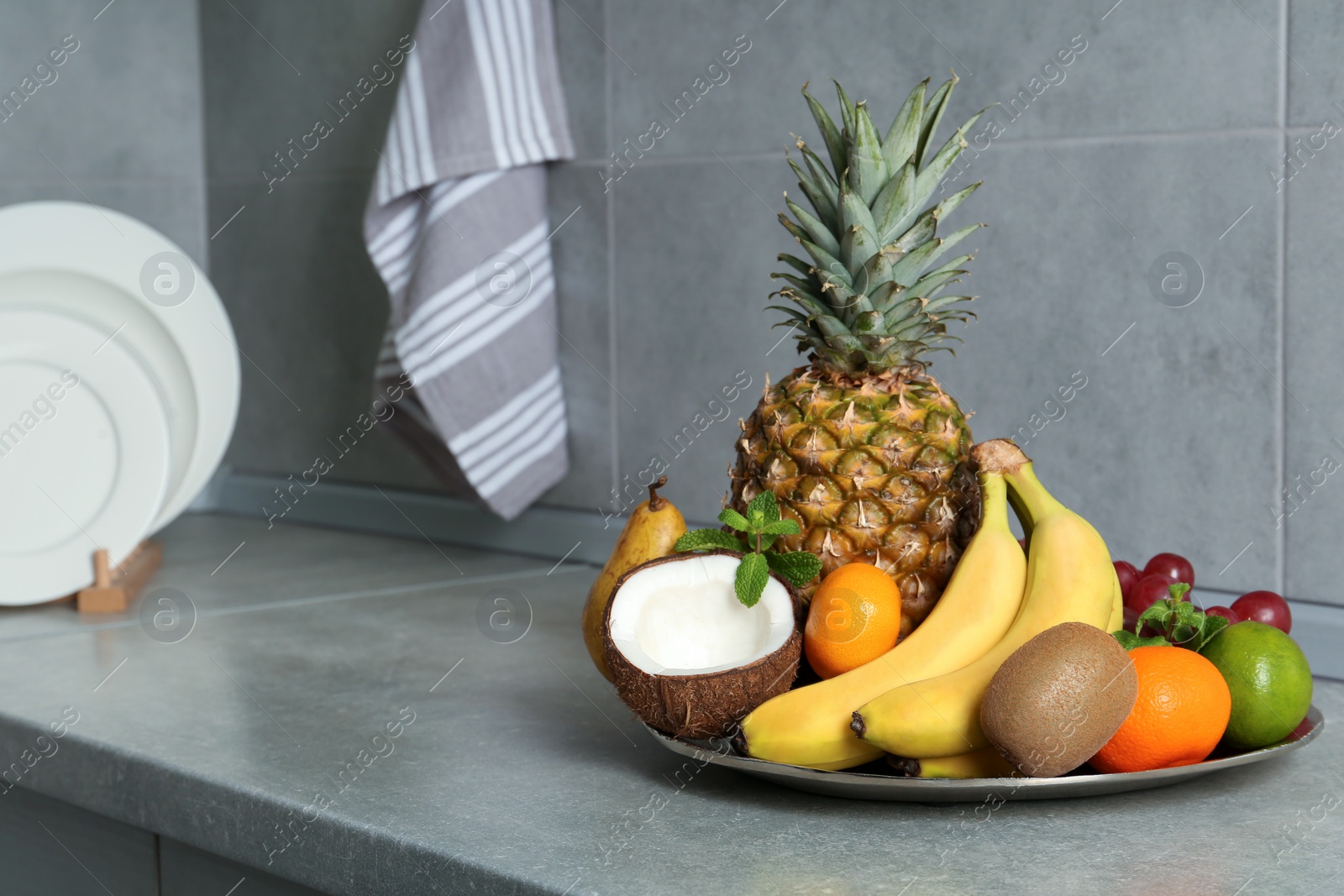 Photo of Plate with different ripe fruits on grey countertop. Space for text