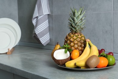 Plate with different ripe fruits on grey countertop. Space for text