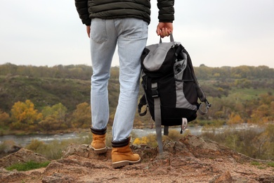 Man wearing stylish hiking boots with backpack on steep cliff, closeup