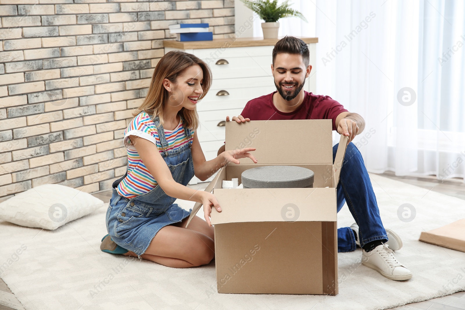 Photo of Young couple opening parcel on floor at home