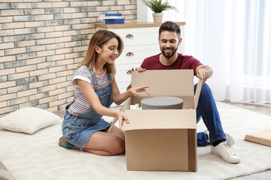 Photo of Young couple opening parcel on floor at home