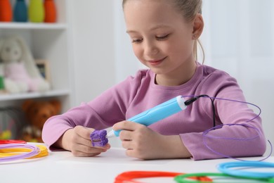 Photo of Girl drawing with stylish 3D pen at white table indoors