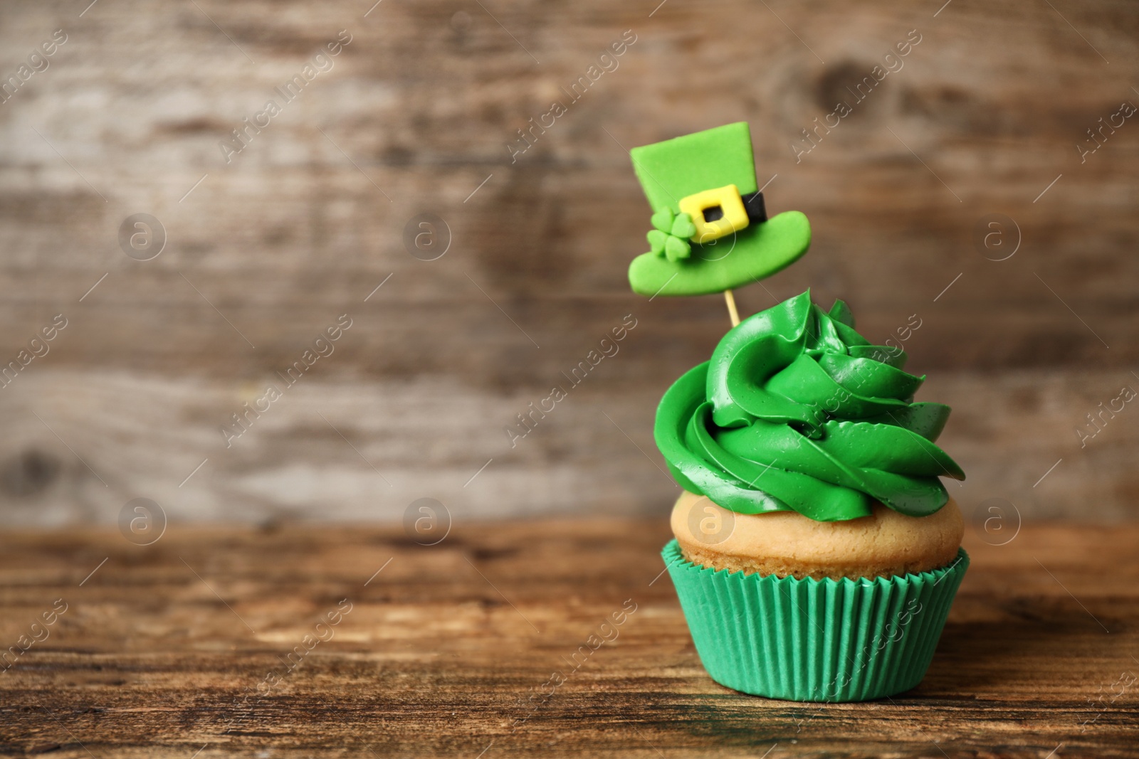 Photo of Decorated cupcake on wooden table, space for text. St. Patrick's Day celebration