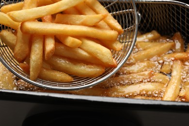 Photo of Delicious freshly prepared french fries in metal strainer, closeup