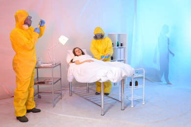 Photo of Paramedics wearing protective suits examining patient with virus in quarantine ward