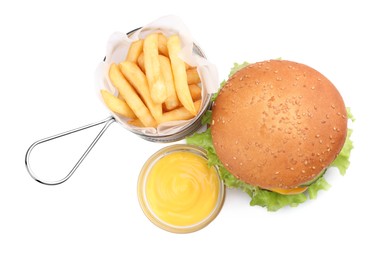 Photo of French fries in frying basket, sauce and tasty burger on white background, top view