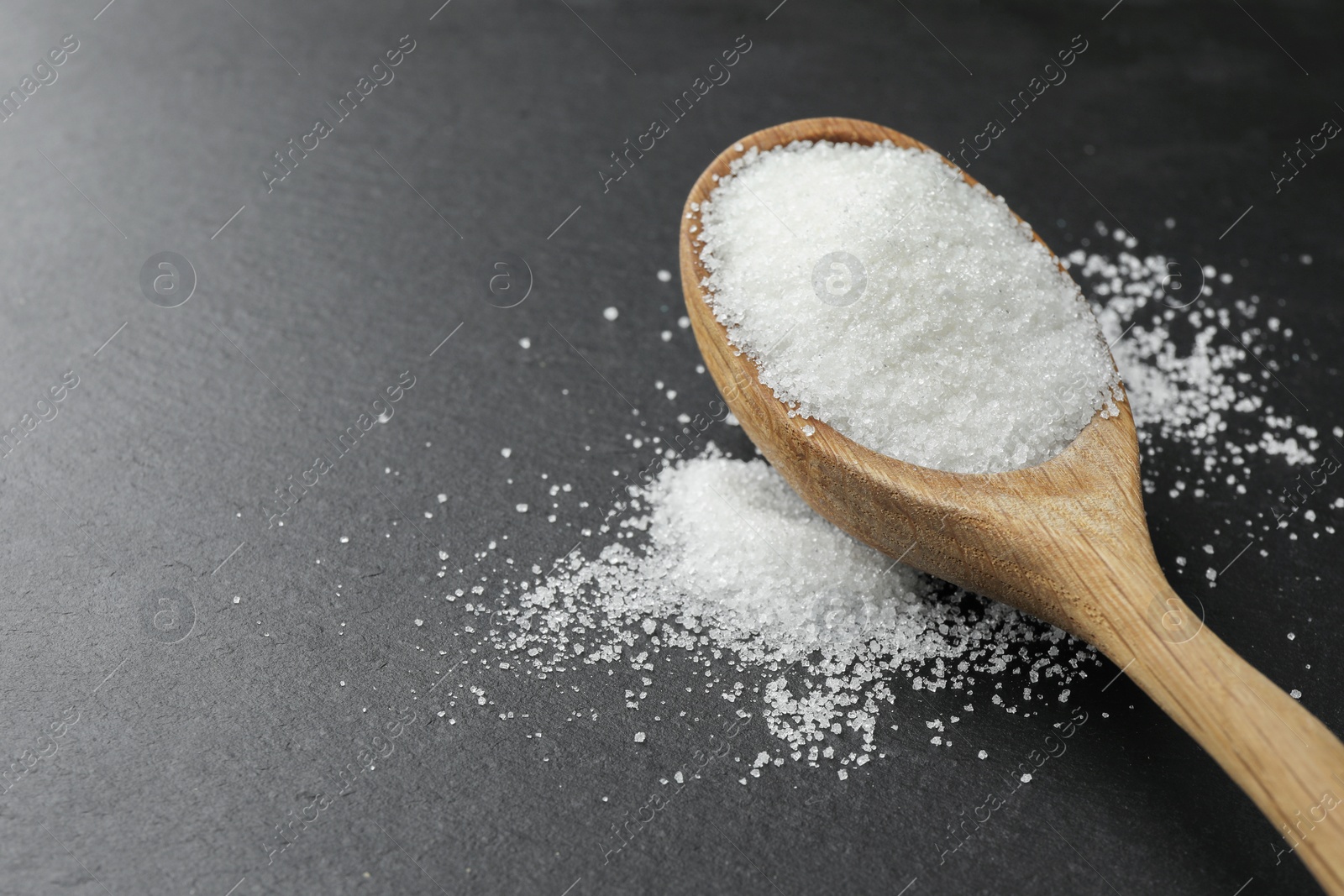 Photo of Spoon with granulated sugar on black table, closeup. Space for text