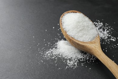 Spoon with granulated sugar on black table, closeup. Space for text