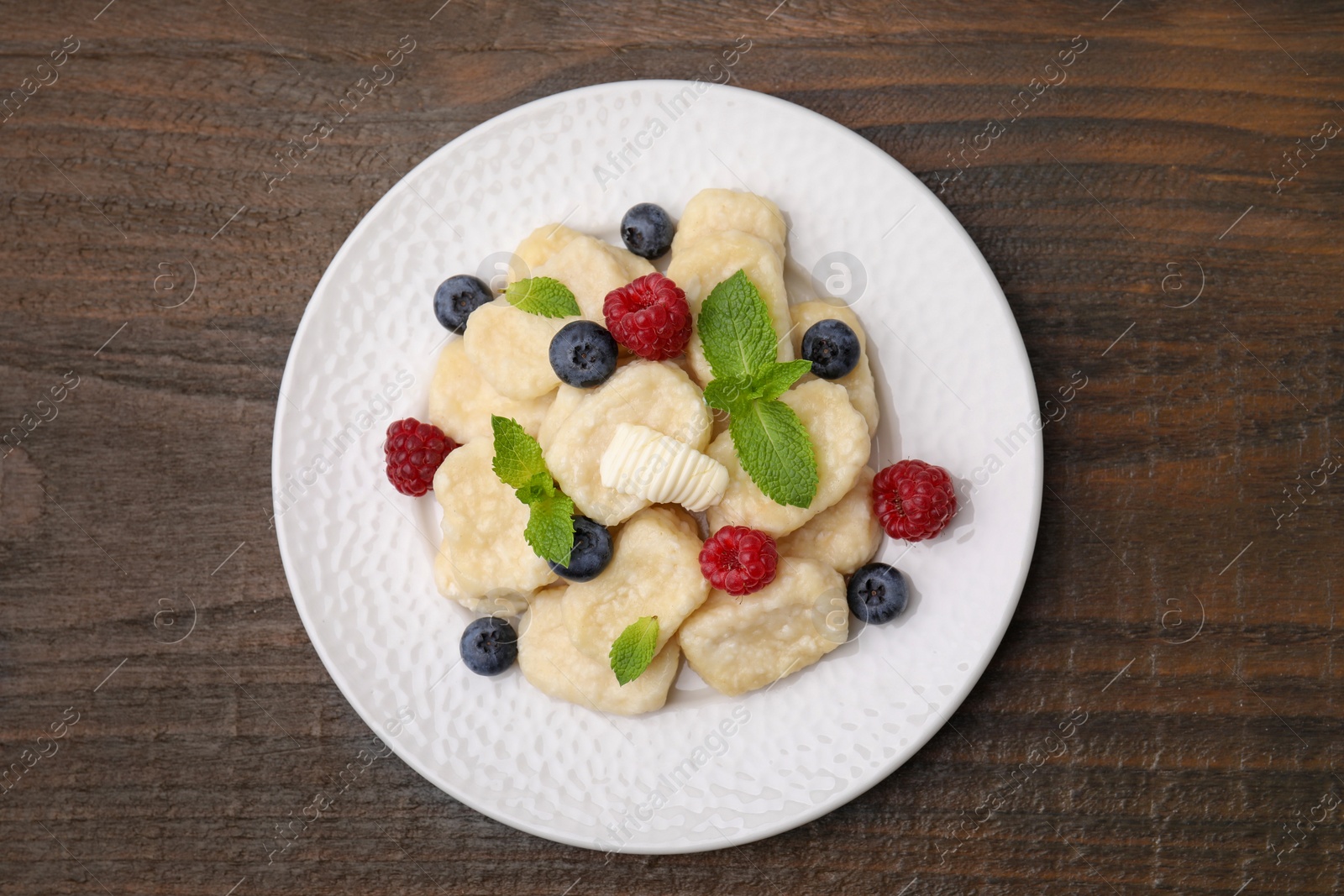 Photo of Plate of tasty lazy dumplings with berries, butter and mint leaves on wooden table, top view