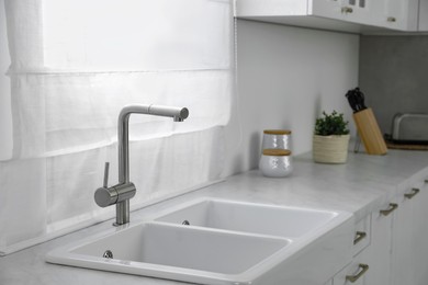 Photo of Modern sink and water tap near window in kitchen. Interior design