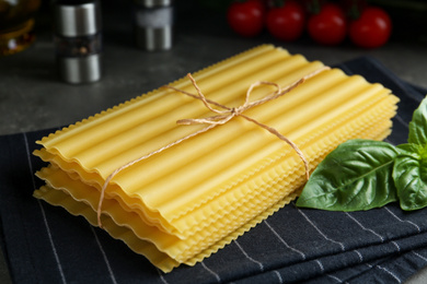 Photo of Uncooked lasagna sheets and basil on table, closeup