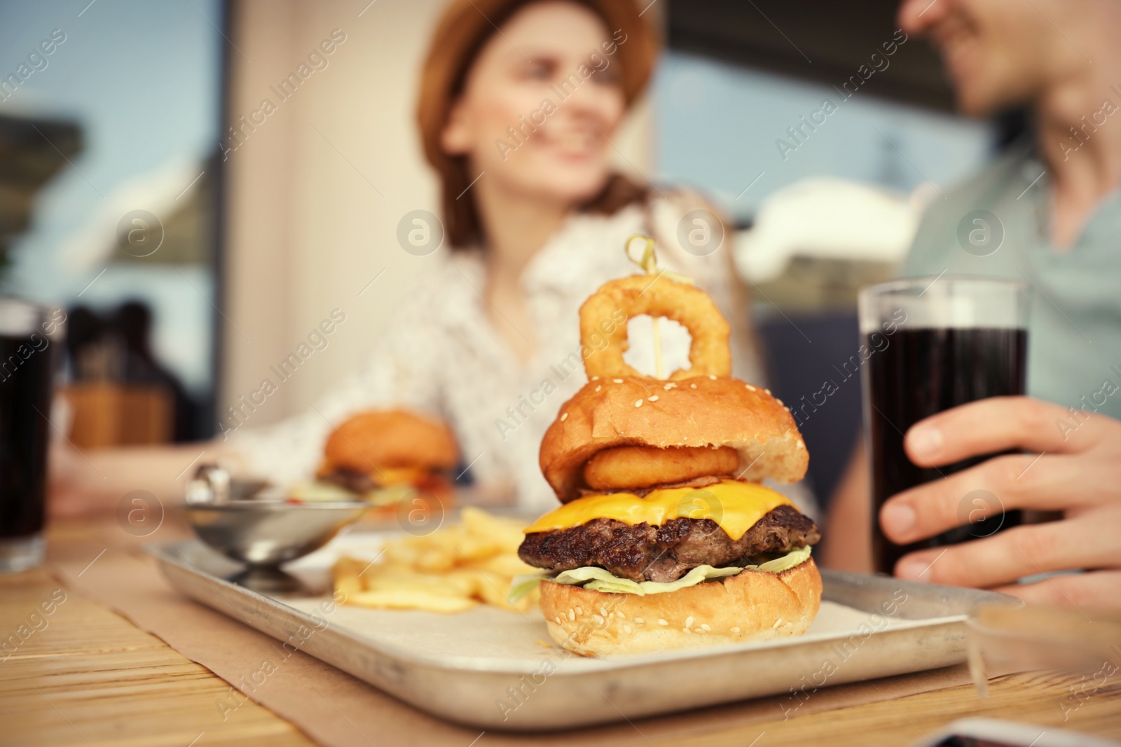 Photo of Young happy couple in street cafe, focus on tasty burger