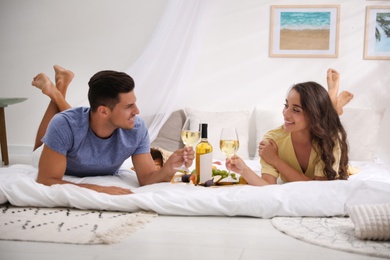 Happy couple with wine and tasty food imitating picnic at home