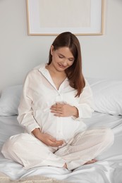 Photo of Happy young pregnant woman in pajamas on bed at home