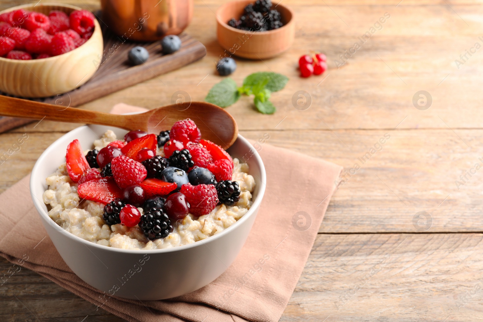 Photo of Bowl with tasty oatmeal porridge and berries served on wooden table. Space for text