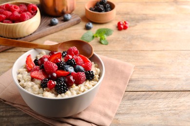 Photo of Bowl with tasty oatmeal porridge and berries served on wooden table. Space for text