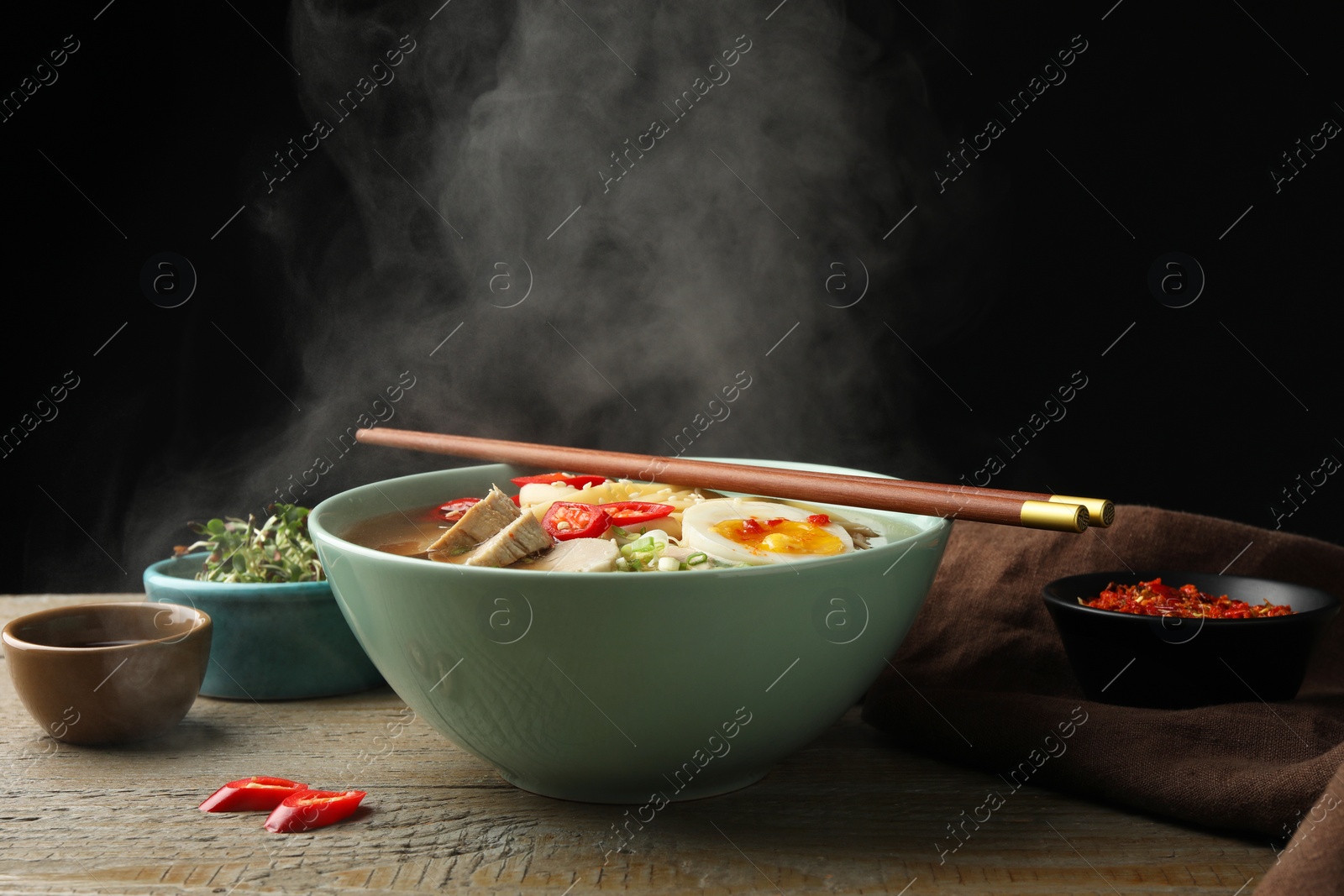 Photo of Delicious ramen in bowl on wooden table against black background, closeup. Noodle soup