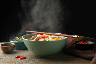 Photo of Delicious ramen in bowl on wooden table against black background, closeup. Noodle soup