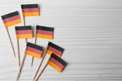 Photo of Small paper flags of Germany on white wooden table, flat lay. Space for text