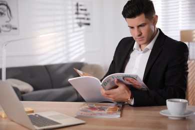 Photo of Man reading magazine at table in office