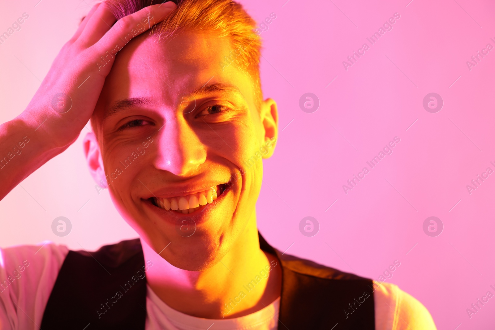 Photo of Stylish young man on pink background in neon lights. Space for text