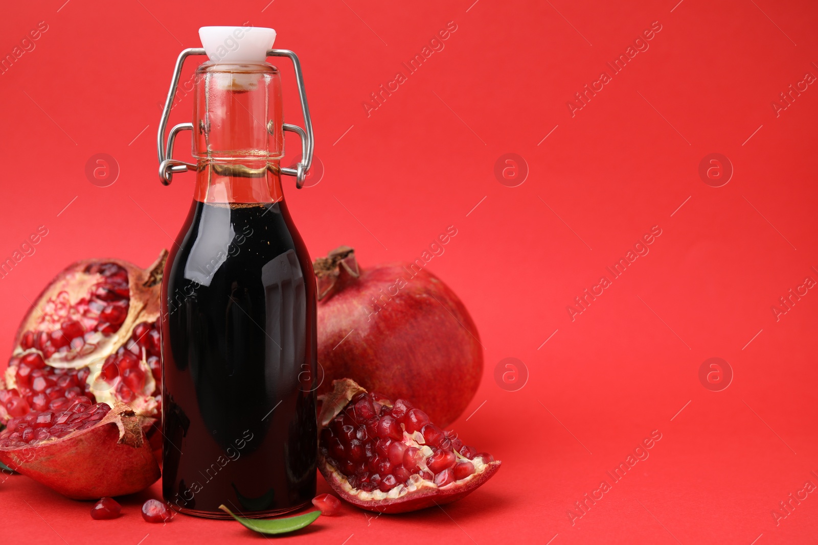 Photo of Tasty pomegranate sauce in bottle and fruits on red background, closeup. Space for text