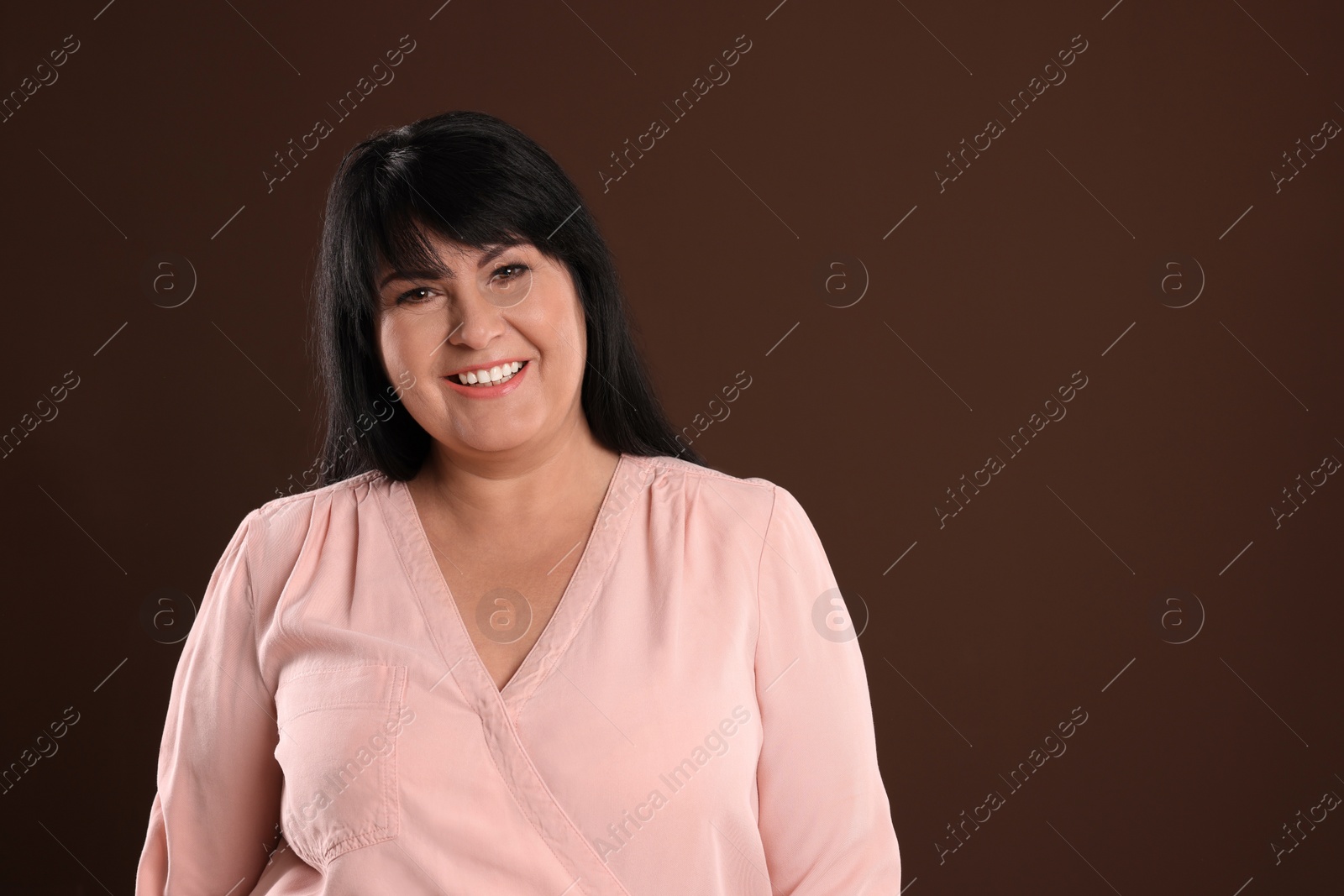 Photo of Beautiful overweight mature woman with charming smile on brown background. Space for text