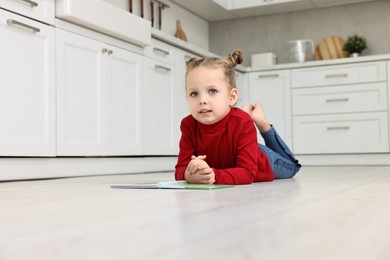 Photo of Cute little girl with book on warm floor in kitchen, space for text. Heating system