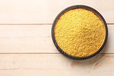 Photo of Millet groats in bowl on light wooden table, top view. Space for text