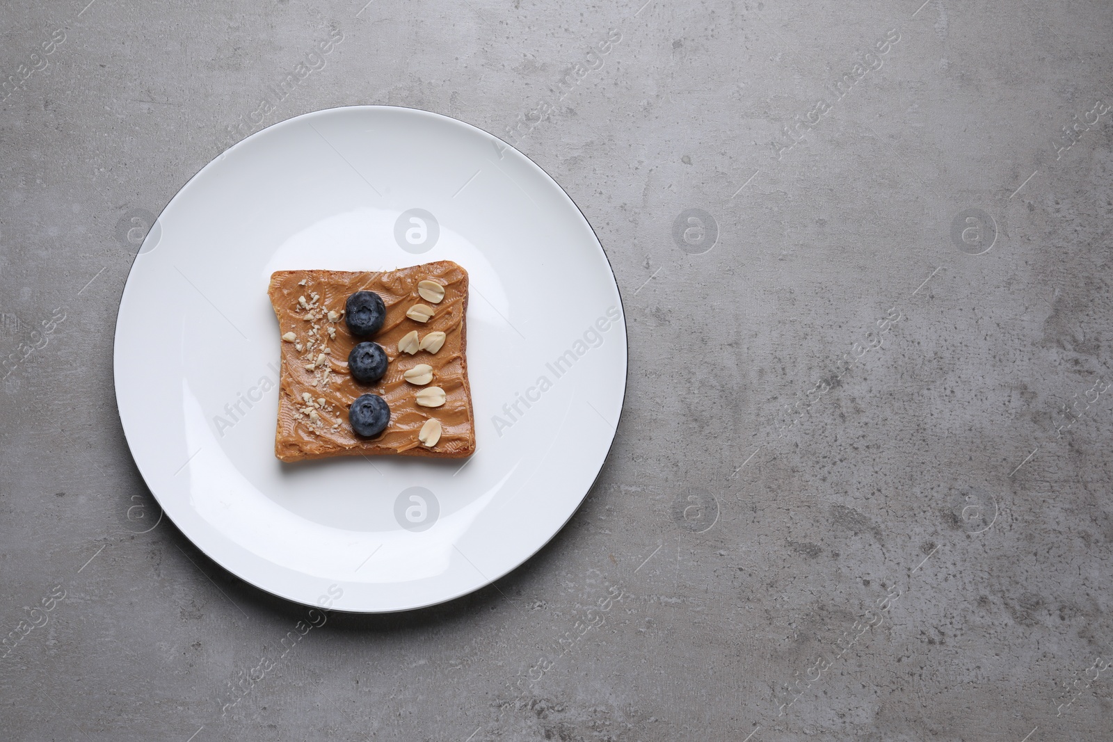 Photo of Toast with tasty nut butter, blueberries and nuts on grey textured table, top view. Space for text