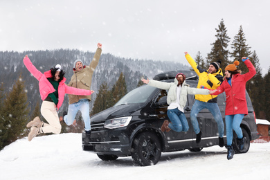 Photo of Happy people jumping near car on snowy road. Winter vacation