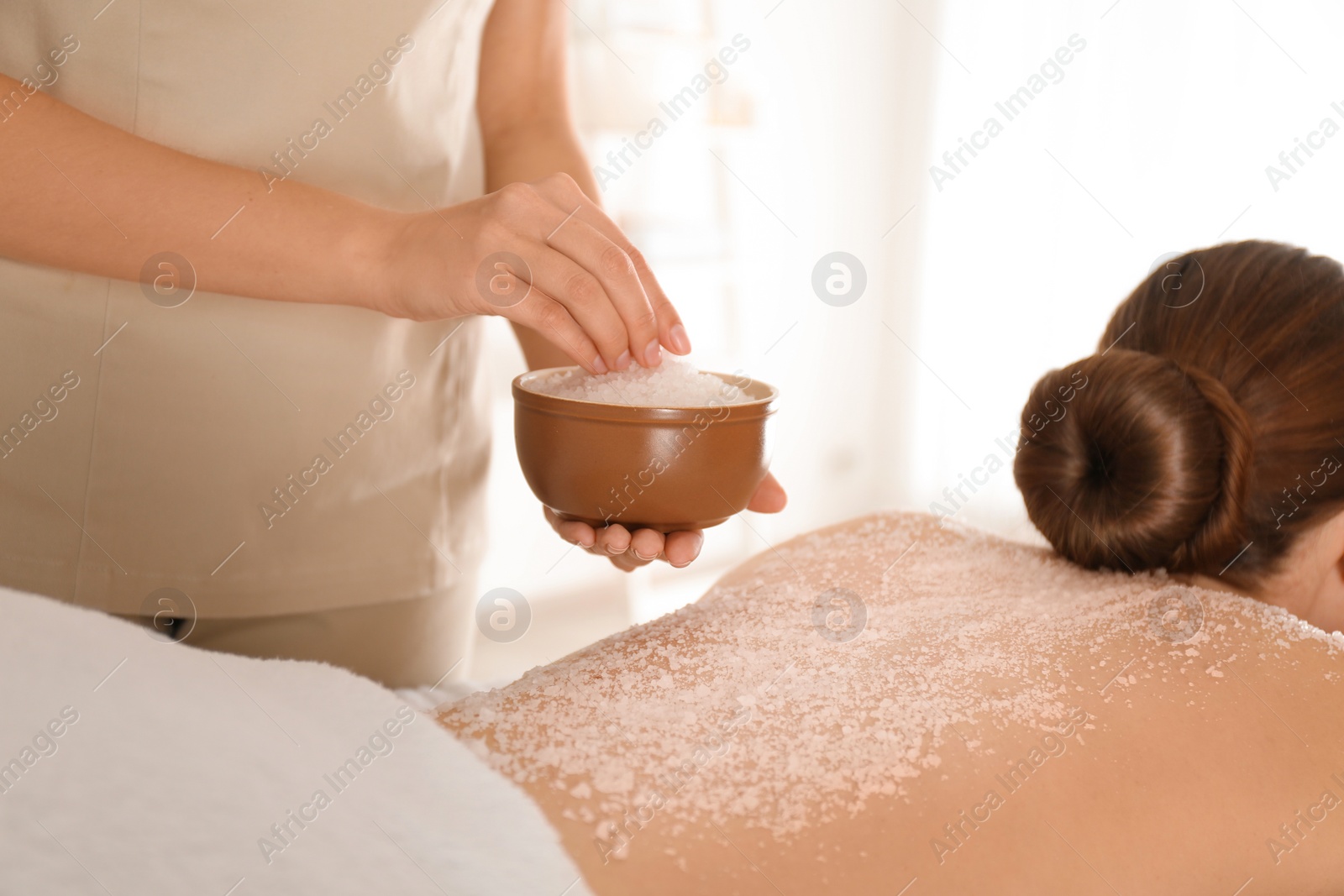 Photo of Young woman having body scrubbing procedure with sea salt in spa salon, closeup