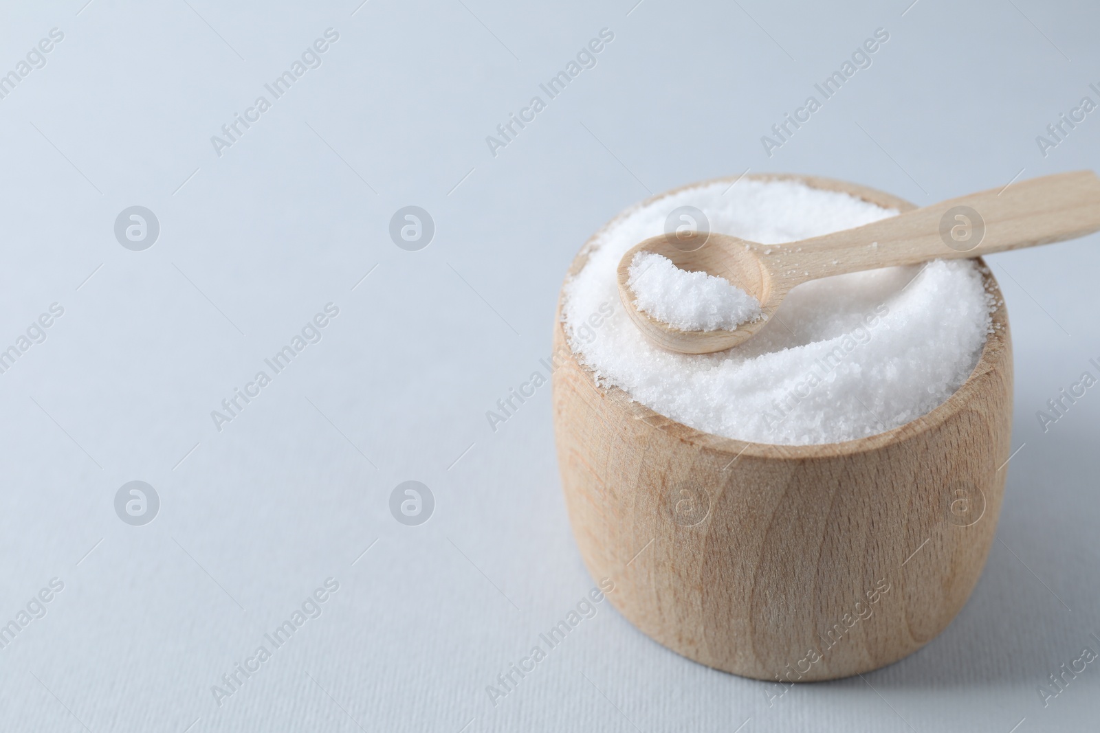 Photo of Organic white salt in bowl and spoon on light grey background, closeup. Space for text