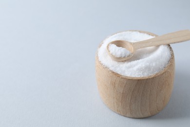 Photo of Organic white salt in bowl and spoon on light grey background, closeup. Space for text