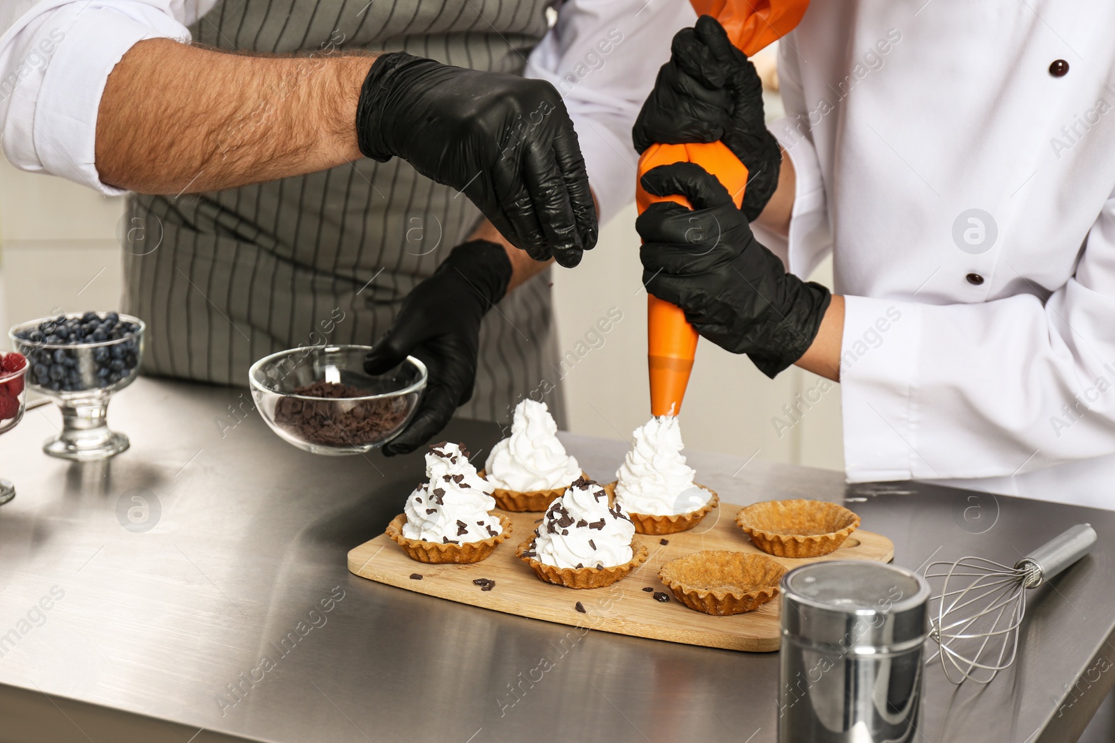 Photo of Pastry chefs preparing desserts at table in kitchen, closeup