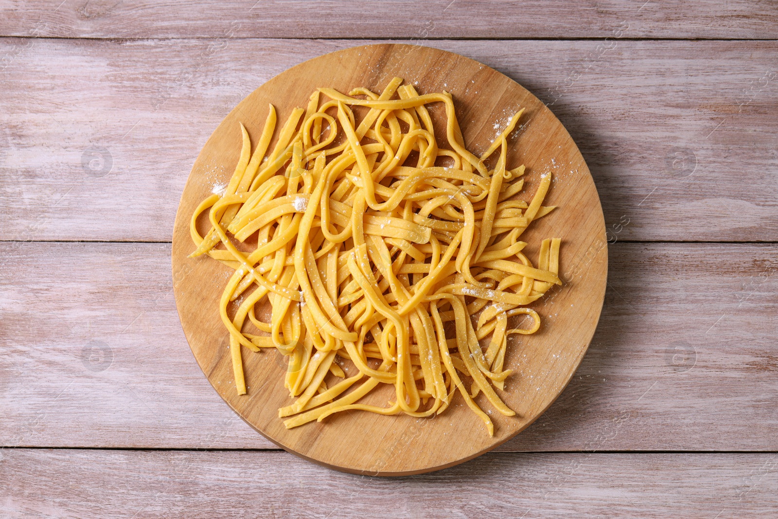 Photo of Board with homemade pasta on wooden table, top view