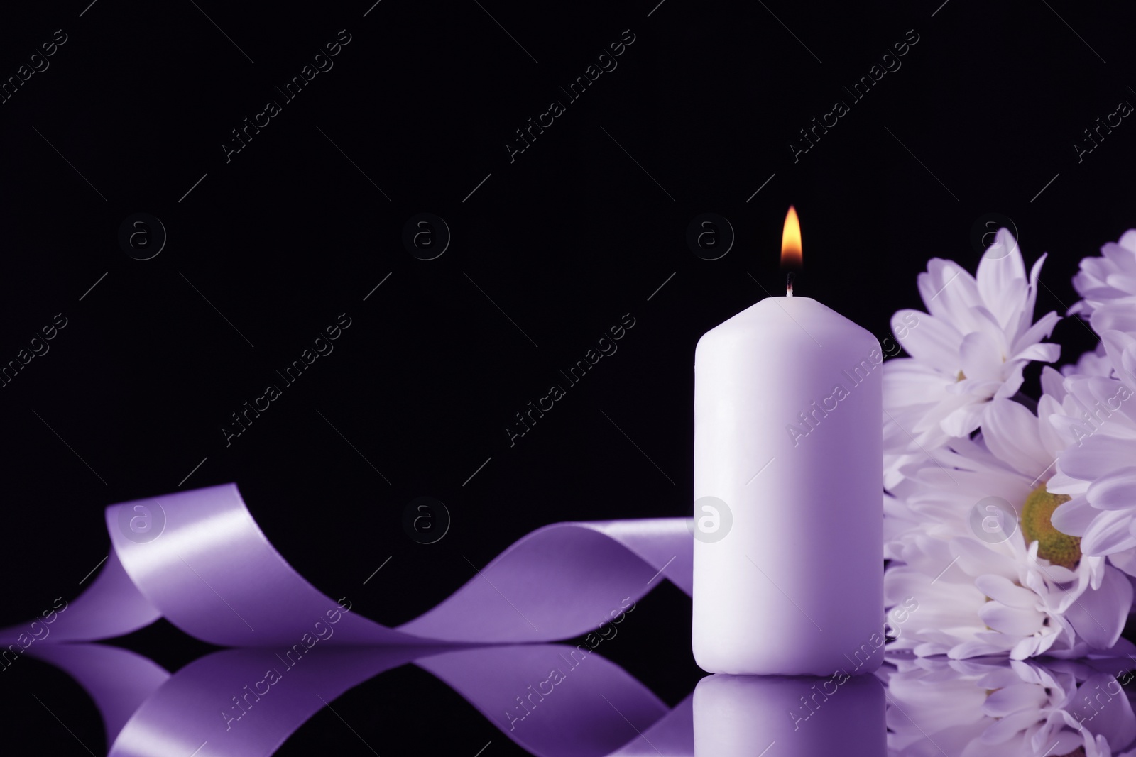 Image of Burning candle, violet chrysanthemum flowers and ribbon on black mirror surface in darkness, space for text. Funeral attributes