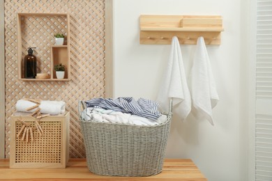 Photo of Wicker basket with dirty laundry on wooden table in bathroom