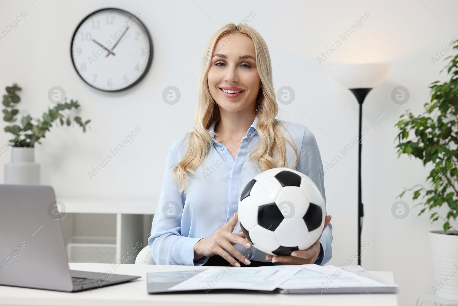 Photo of Happy woman with soccer ball at table in office