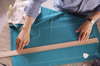 Tailor working with cloth at table in atelier, top view