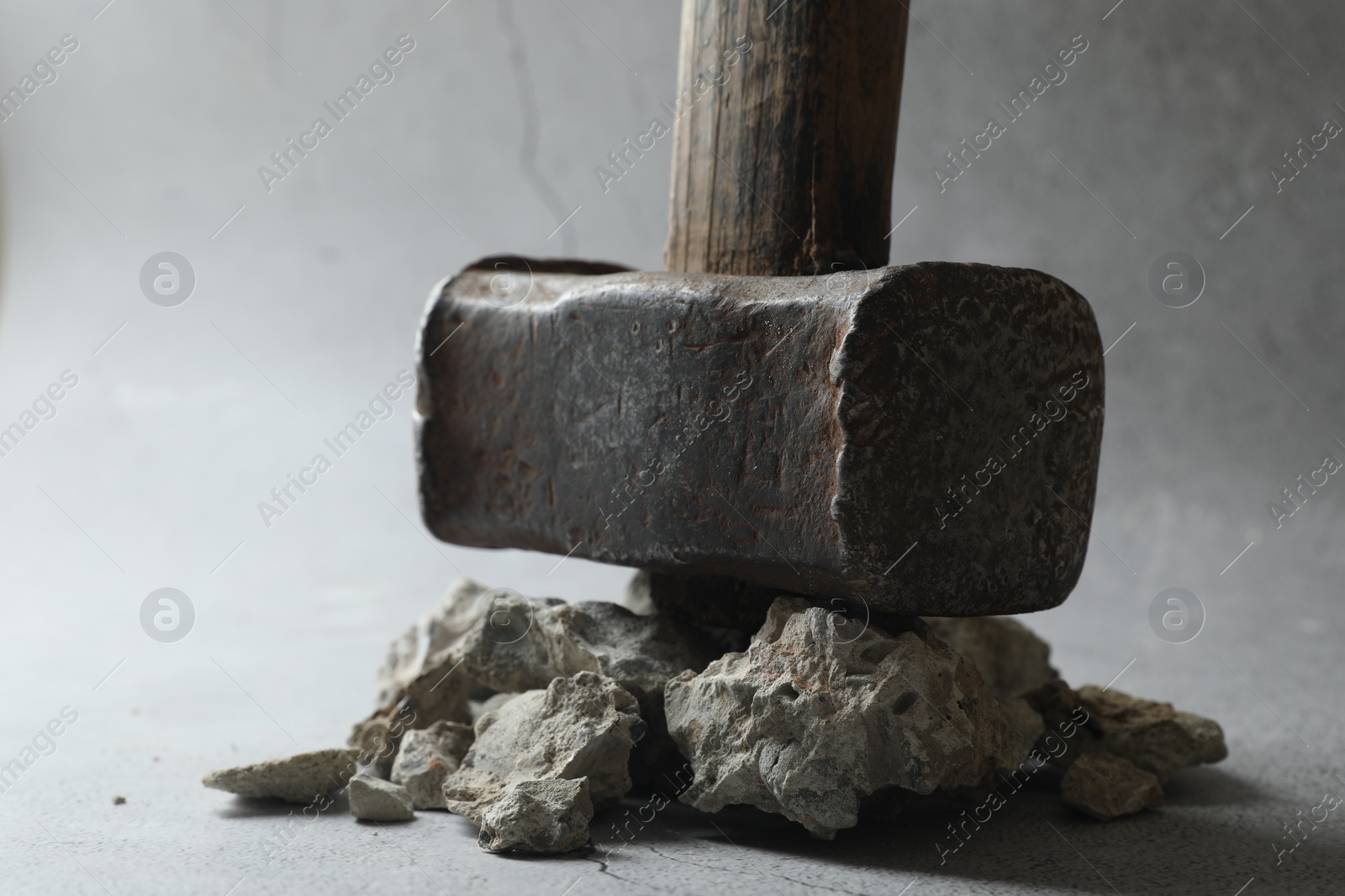 Photo of One sledgehammer and pieces of broken stones on grey background, closeup