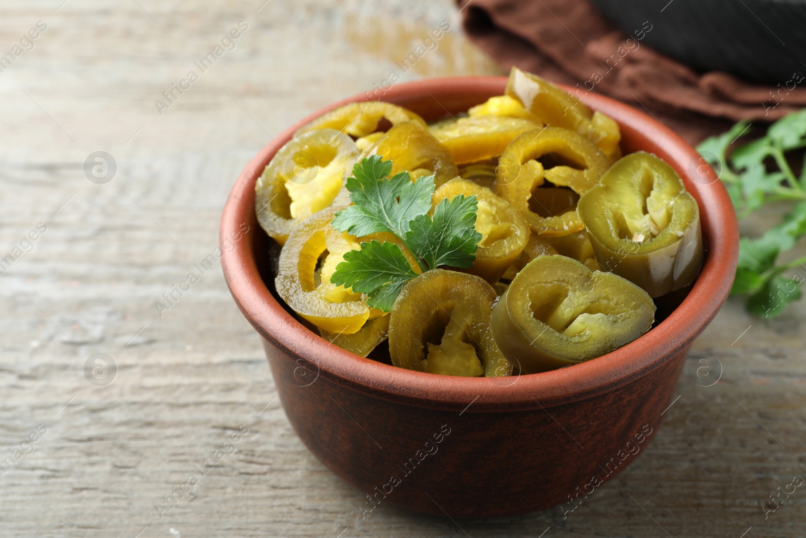 Photo of Bowl with slices of pickled green jalapeno peppers on wooden table