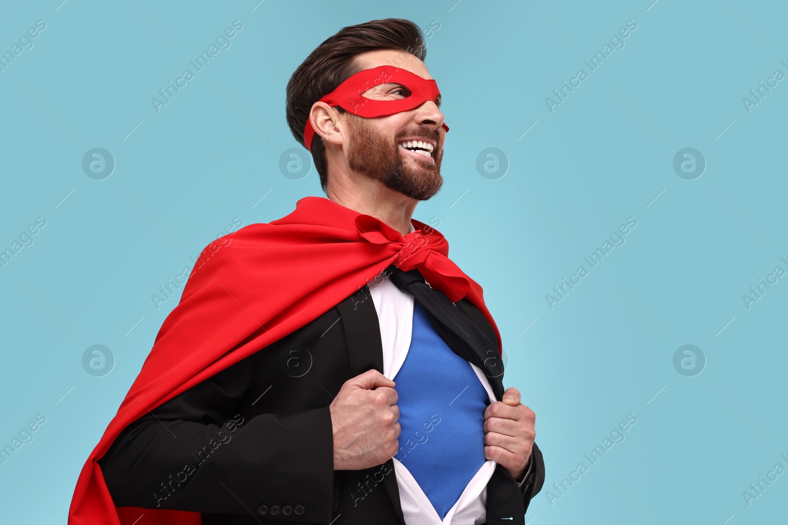 Photo of Happy businessman wearing superhero costume under suit on light blue background. Space for text