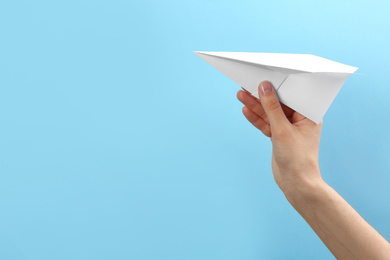 Woman holding paper plane on light blue background, closeup. Space for text