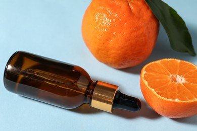 Photo of Aromatic tangerine essential oil in bottle and citrus fruits on light blue table, closeup