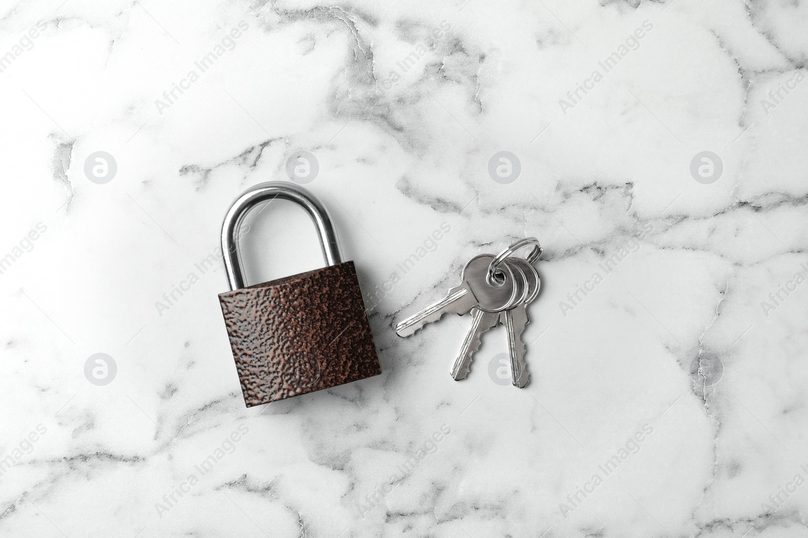 Photo of Steel padlock and keys on white marble background, top view. Safety concept